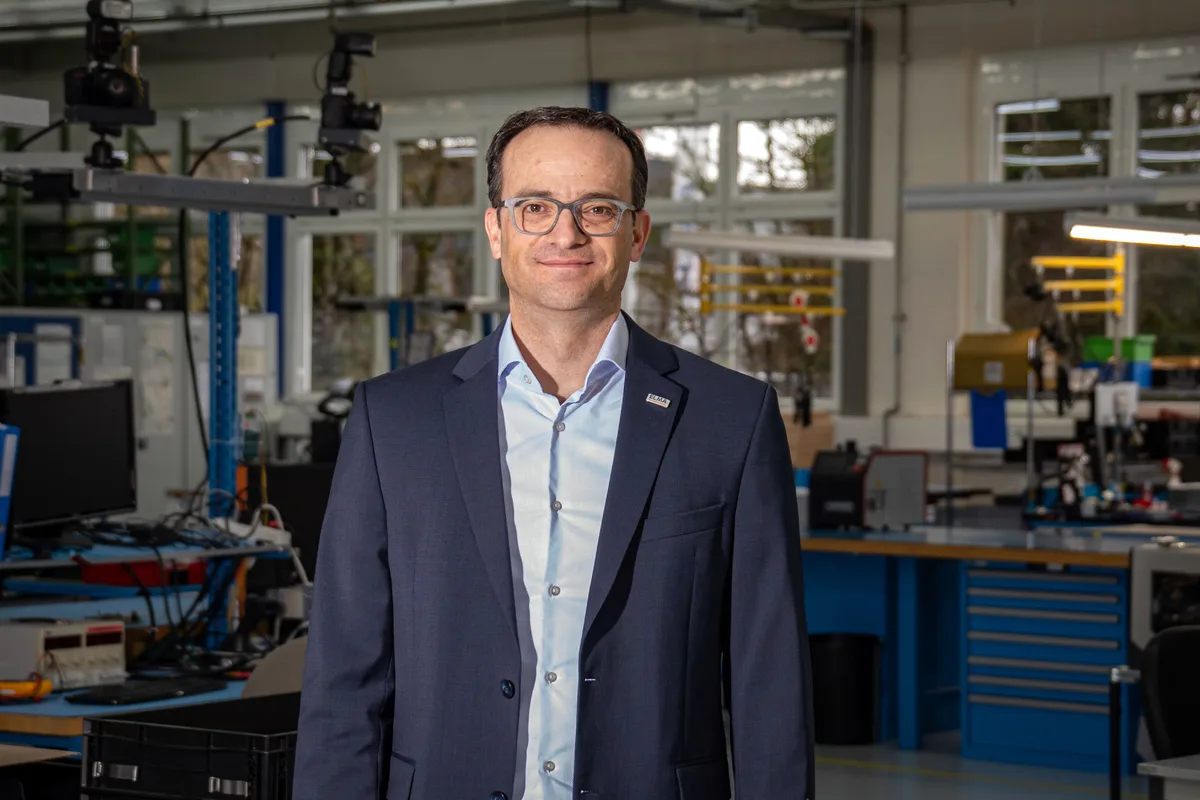 Elma-CEO Thomas Herrmann in der Produktionshalle in Wetzikon. Er trägt einen dunkelblauen Anzug und ein hellblaues Hemd.